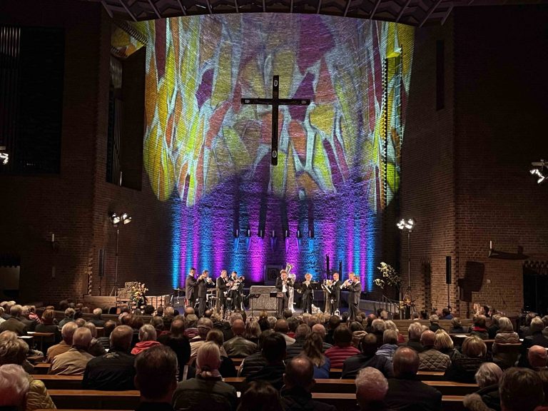 Eine Band spielt in einer Kirche, in der das Kirchenschiff atmosphaerisch ausgeleuchtet wird.